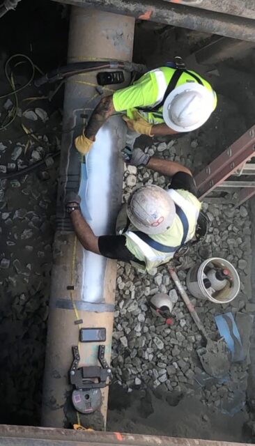 Two workers working on the pipe in the excavation